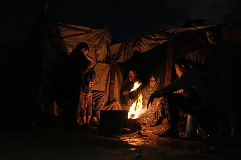 Yerlerinden edilmiş Filistinliler Gazze'deki bir çadır kampında ateşin etrafında ısınıyor, 18 Ocak 2026.